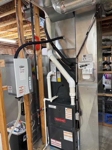 Goodman HVAC system installed in a basement with visible ductwork and pipes.