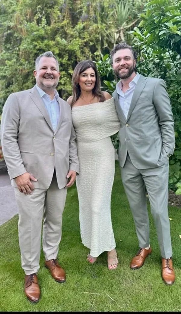 Same-sex men groomsmen with their woman officiant between them who is dressed in a white dress.