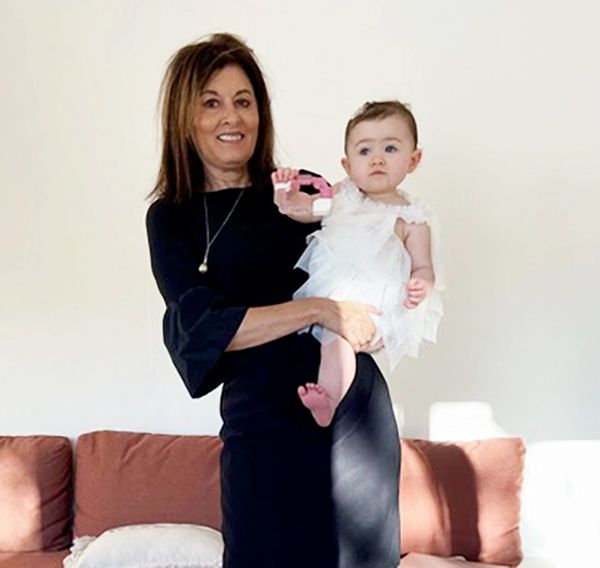 Diana Cruz Navratil, shown in a black dress holding a little girl in a white dress. Orange couch.