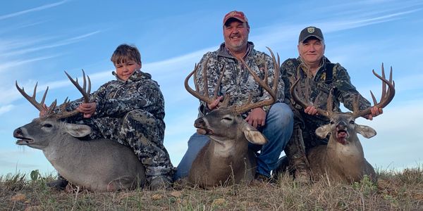 This is an image of three people with three whitetail deer.