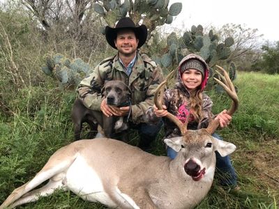 This is an image of a man, a girl, and a dog with a whitetail deer.