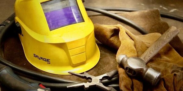 Welding helmet, gloves, and tools arranged on a surface.