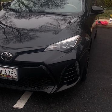 Black Toyota car parked in a residential area with reflections of tree branches.