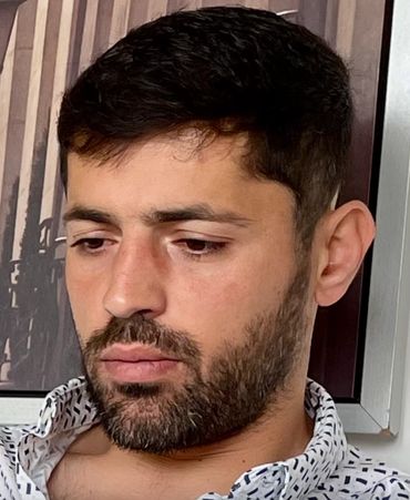 Young man with dark hair and beard looking down thoughtfully.