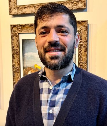 Smiling man with a beard in a checkered shirt and dark sweater.