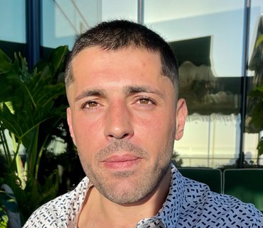 Young man with short hair and patterned shirt bathed in sunlight.