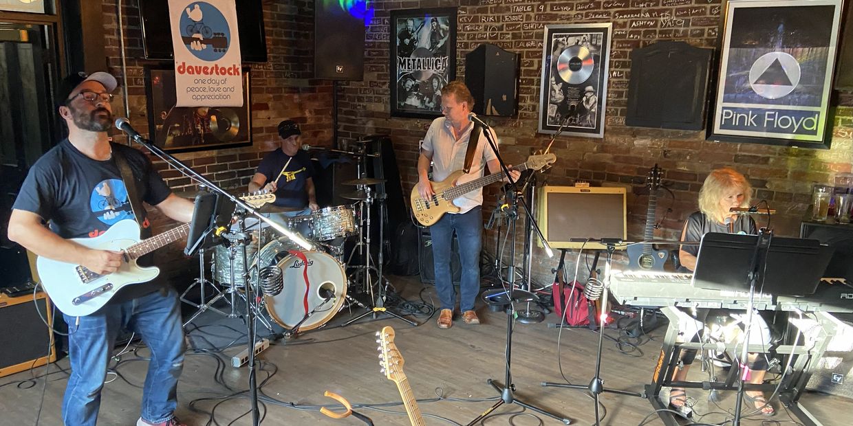 Band performing live in an intimate venue with posters of Metallica and Pink Floyd.