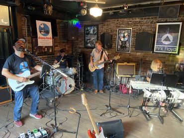 Band performing live in an intimate venue with posters of Metallica and Pink Floyd.