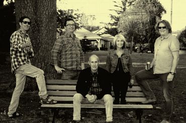 A group of five adults posing outdoors around a park bench with 'Look Out Nelson' text.