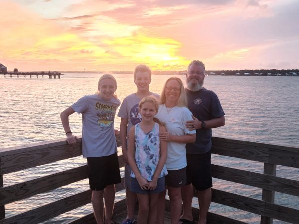 Family of five posing on a wooden pier at sunset by the water.