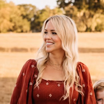 Smiling blonde woman in a red dress outdoors.