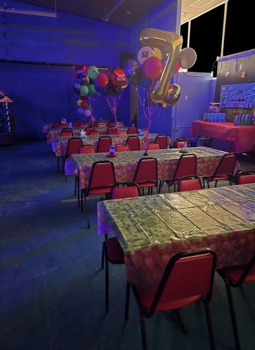 Tables decorated with balloons and covered in plastic tablecloths for a birthday party.