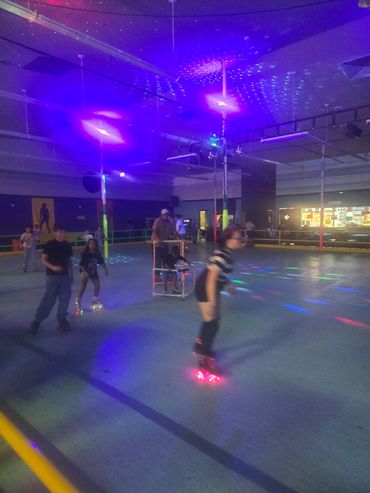 People roller skating in a dimly lit rink with colorful lights.