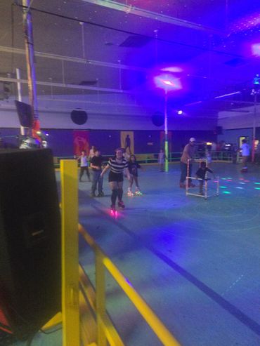People skating at an indoor roller rink with colorful lights.