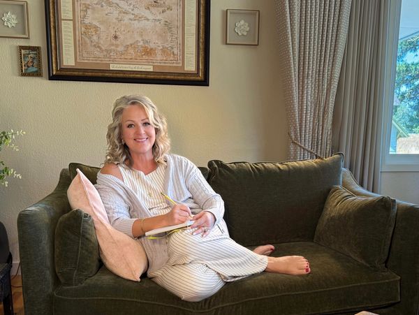 Smiling woman sitting on a green sofa, writing in a notebook.