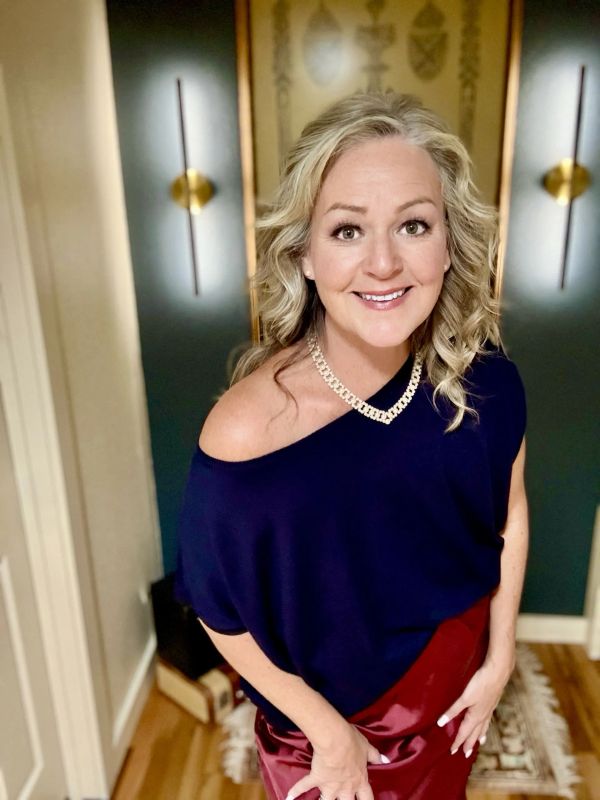 Smiling woman in elegant outfit with curly blonde hair.