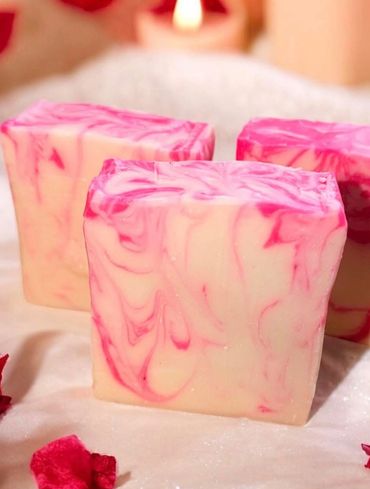 Three pink and white marbled soap bars with rose petals and lit candles.