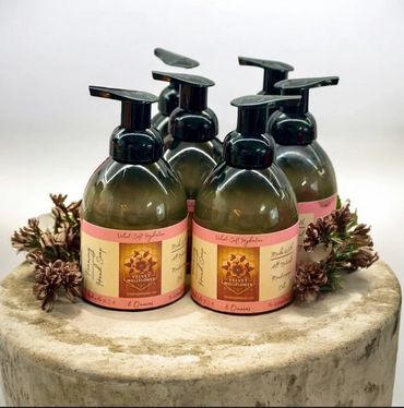 Set of five Velvet Wallflower foaming hand soap bottles on a round stone surface.