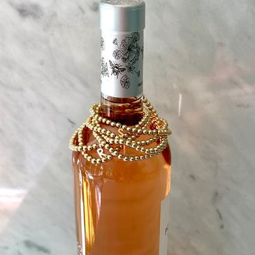 Three gold relationship status bracelets on a rosé wine bottle.