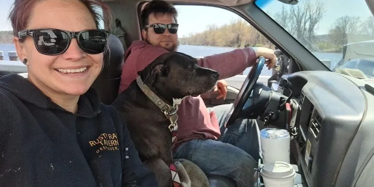 Couple and their dog enjoying a sunny day in the car near a lake.