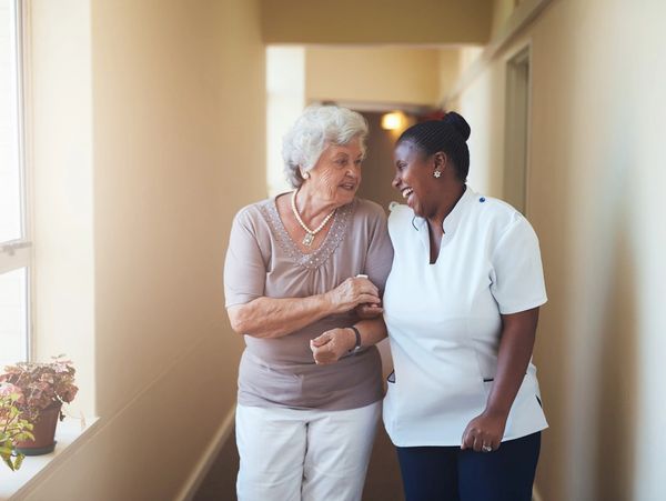 Portrait of happy female caregiver and senior woman walking together at home.