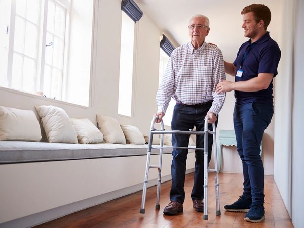 Senior man using a walking frame with male nurse at home