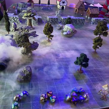 Tabletop RPG setup with terrain, trees, buildings, and dice on a grid.