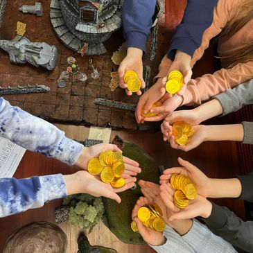 Hands holding gold coins over a tabletop game setup.