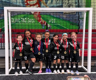 Young soccer players with medals pose happily in front of a goalpost.