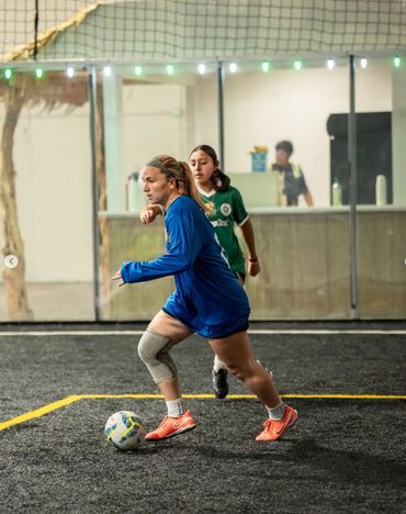 Two women playing indoor soccer, one in blue controlling the ball.