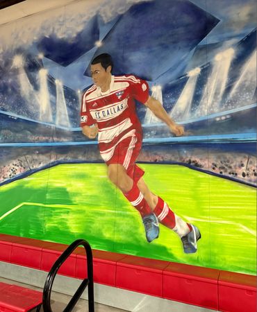 Mural of an FC Dallas soccer player in action on a stadium field.