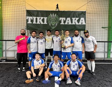 Soccer team posing with a trophy under a Tiki Taka banner.