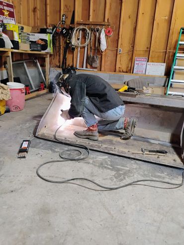 Person welding metal in a workshop wearing protective gear.