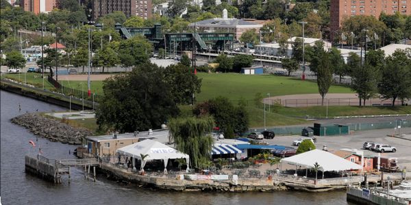 A waterfront park area with tents and a green field in the background.