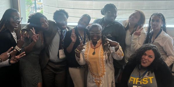 Group of people smiling and making peace signs indoors near a window.