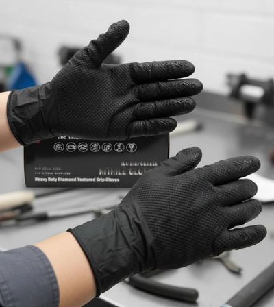 Hands wearing black textured grip gloves in a workshop setting.