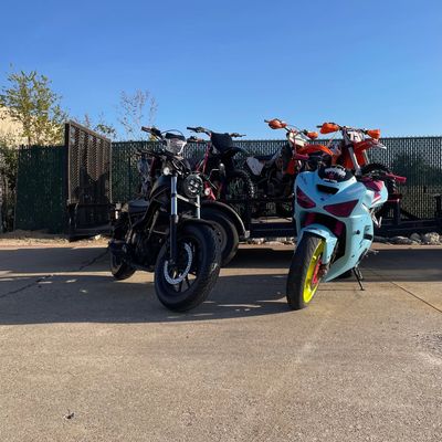 Two motorcycles parked in front of a trailer carrying dirt bikes under a clear blue sky.