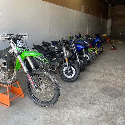 A row of parked motorcycles including a green dirt bike indoors.