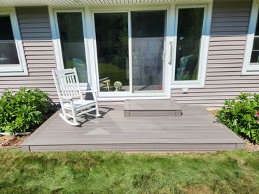 Small wooden deck with a white rocking chair outside a house.