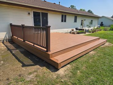 Newly built wooden deck attached to a house with railing on one side.