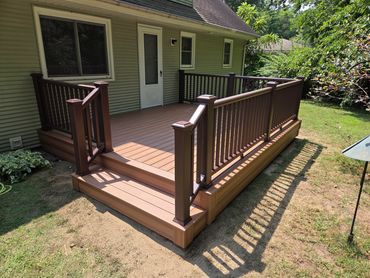Newly built wooden deck with brown railings and steps attached to a house.