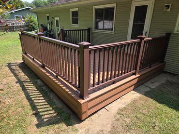 Newly built wooden deck with brown railings attached to a house.