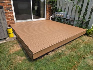 A newly painted brown wooden deck outside a brick house with a sliding door.