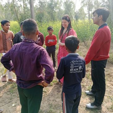 A group of children and a woman stand outdoors, engaged in conversation.