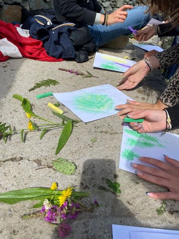 People making leaf rubbings with chalk on paper outdoors.