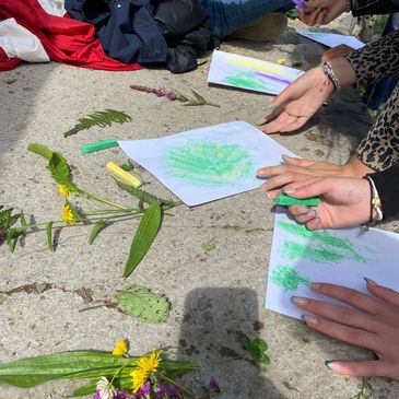 Hands creating leaf rubbings with crayons and flowers outdoors.