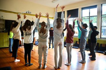 Students standing in a circle raising their arms during a classroom activity.