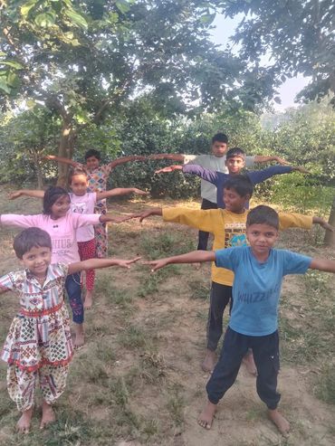 Children standing outdoors in a line with arms outstretched, smiling.