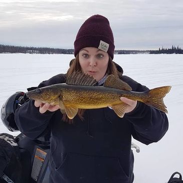 Woman proudly holding a large fish on a snowy landscape.