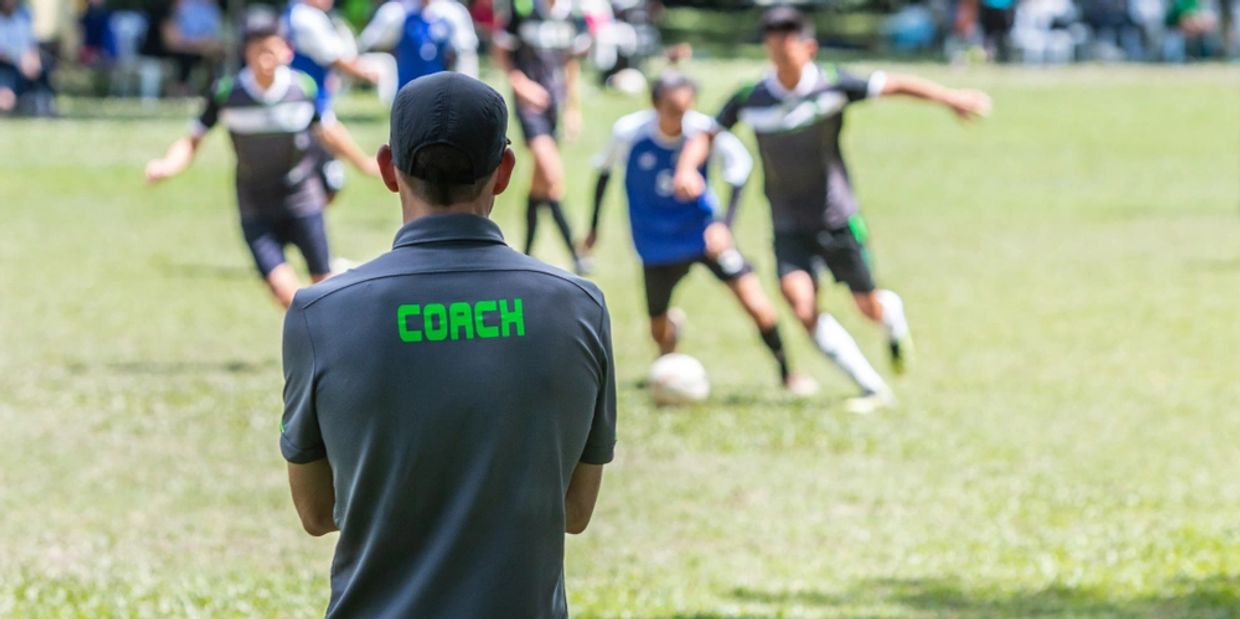 Male soccer or football coach in gray shirt with word COACH written on back